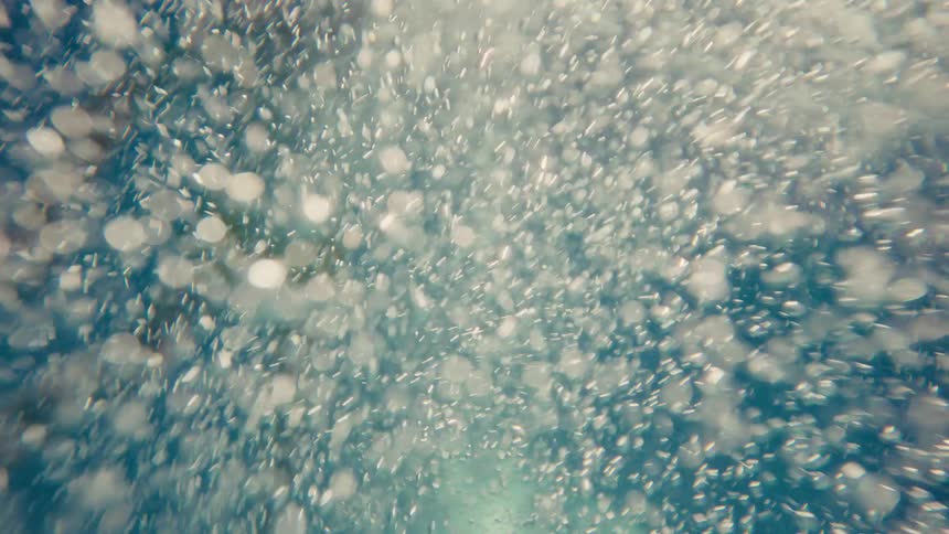 Chaotic and mesmerizing view of countless air bubbles swirling and rising through blue water from an underwater perspective