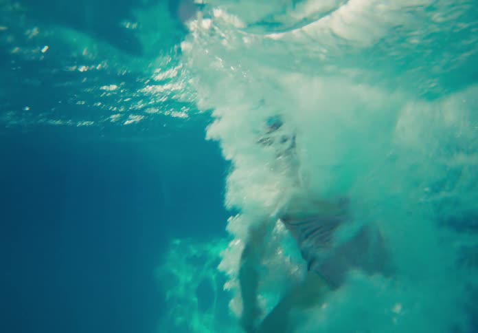 Child jumps into a bright outdoor swimming pool with an underwater splash on a sunny day