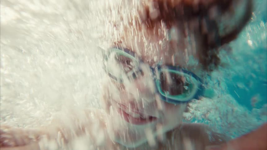 Slow motion POV of a joyful boy with goggles being submerged into a swimming pool by his parent