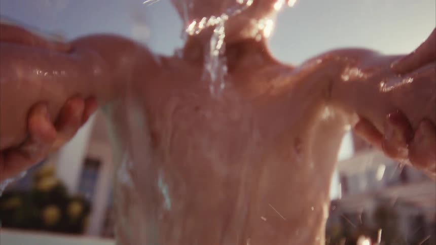 Close-up underwater and overwater view of a smiling boy in goggles being playfully lifted in and out of a pool in slow motion