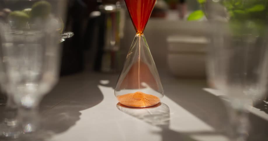 An elegant glass hourglass with vibrant orange sand measures the steady passage of time in the warm sunlight