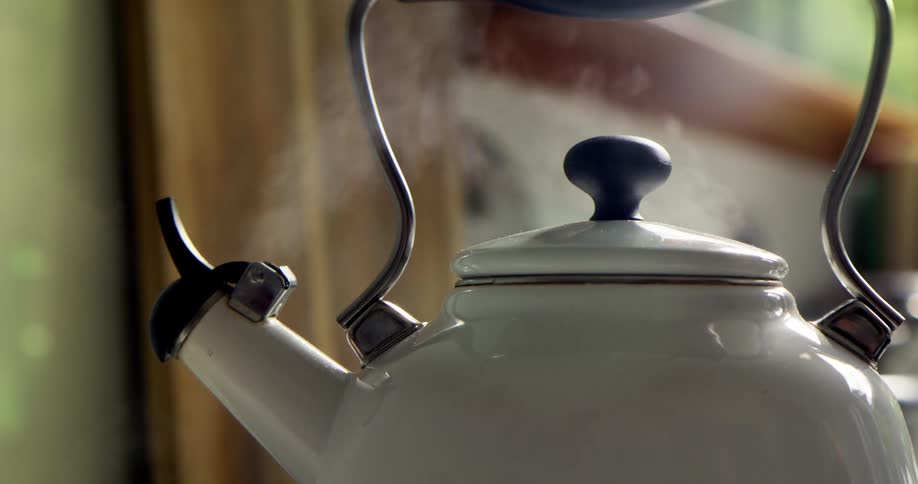 A classic white kettle gently lets off steam as it comes to a boil in a sunlit kitchen