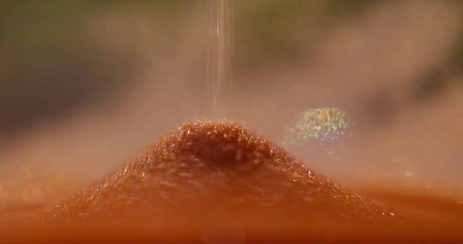 A seamless loop of a macro close-up shot shows shimmering orange sand pouring through an hourglass