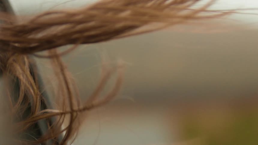 Close-up slow motion shot of a woman's brown hair blowing in the wind reveals a blurry mountain landscape