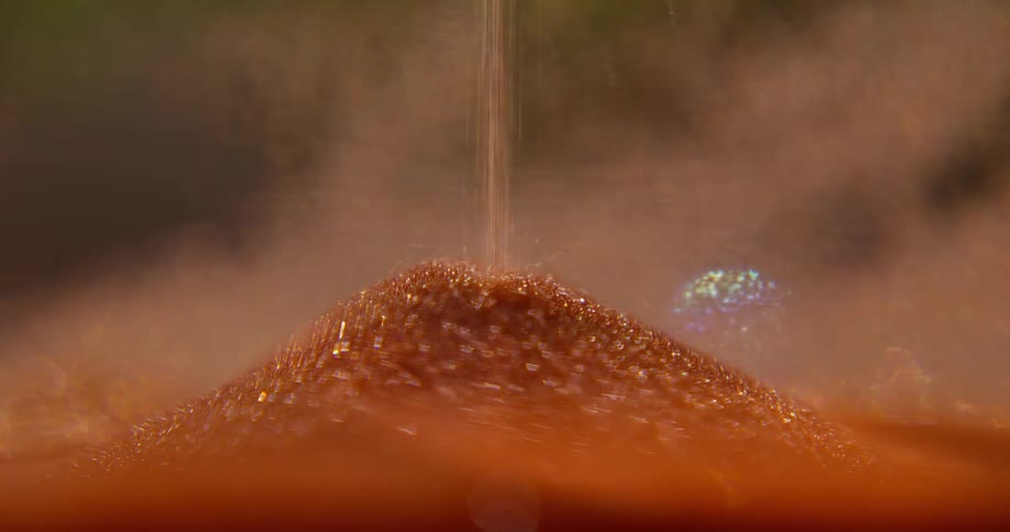 An extreme close-up shot shows shimmering orange sand falling inside an hourglass, creating a mound as time passes
