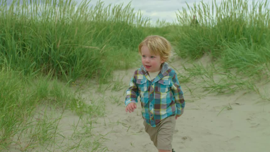 Slow motion shot of an adorable toddler running with joy through sand dunes on an overcast day