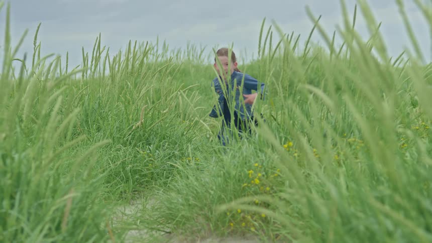 A happy young girl smiles as she runs through a field of tall green grass towards the camera in slow motion