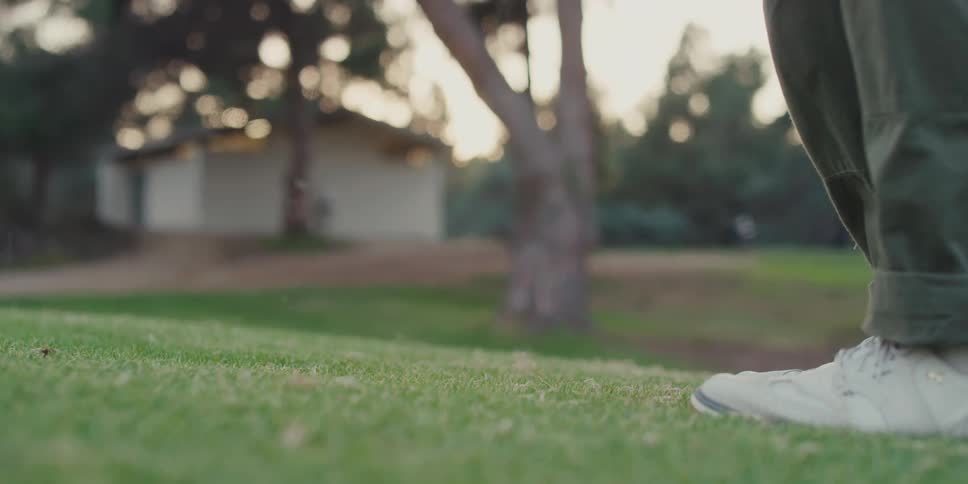 A slow-motion close-up shows a golfer hitting a golf ball with an iron on a lush green course at sunset