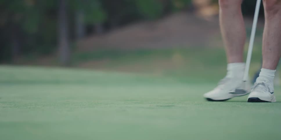 In a slow-motion close-up, a golfer sinks a putt on a manicured green and walks over to retrieve the ball from the cup