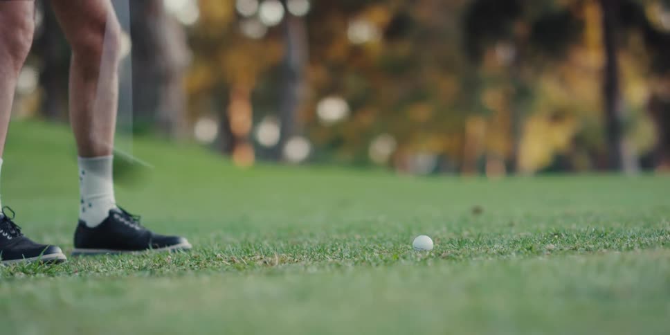 Low-angle slow motion shot of a golf club hitting a golf ball on a green fairway