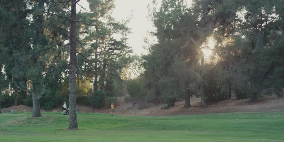 Wide shot of a golfer practicing their swing in slow motion at sunset on a lush green course