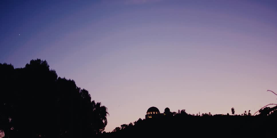 The iconic Griffith Observatory is revealed in silhouette against a serene purple and blue twilight sky