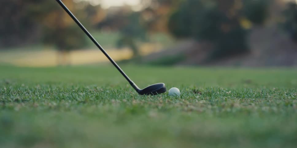 A golf club hits a golf ball on a green fairway in a dramatic super slow-motion close-up