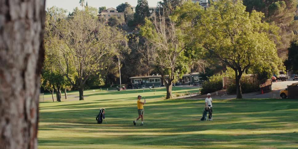 A man in a yellow shirt takes a powerful golf swing in slow motion on a beautiful sunny day at the course