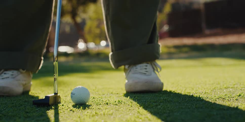 Close up of a golfer lining up their shot and hitting a golf ball with a putter in slow motion on a sunny day