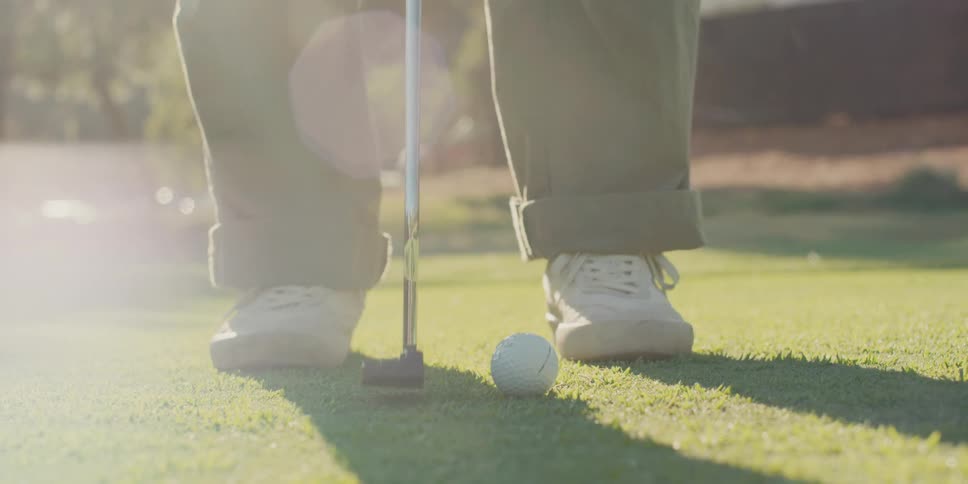 Low-angle slow-motion shot of a person putting a golf ball on a sunny green with a nice lens flare