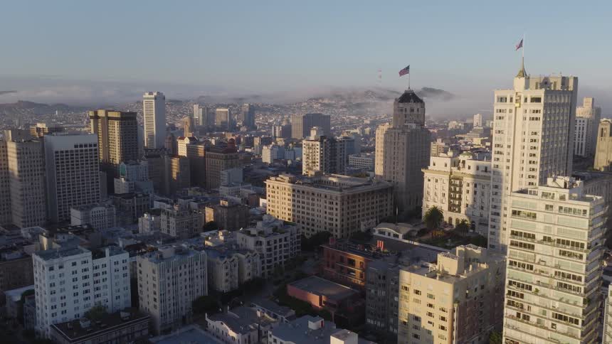 A serene aerial view of downtown San Francisco at sunrise, with golden light illuminating the buildings and fog covering the distant hills