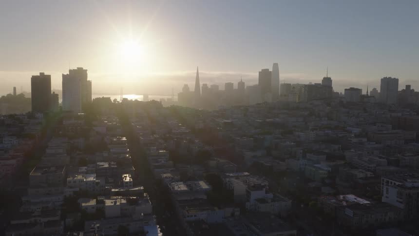 An aerial view of the San Francisco skyline as the sun rises over the city, casting a golden haze