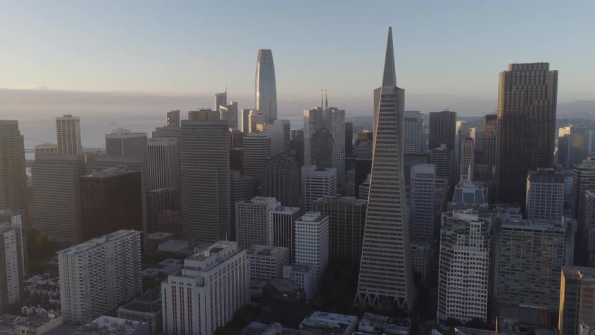 An aerial view reveals the iconic downtown San Francisco skyline, including the Transamerica Pyramid and Salesforce Tower, during a hazy sunrise