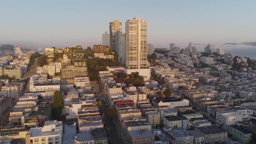 Aerial view flying over the dense urban landscape of San Francisco towards tall buildings during a golden sunrise