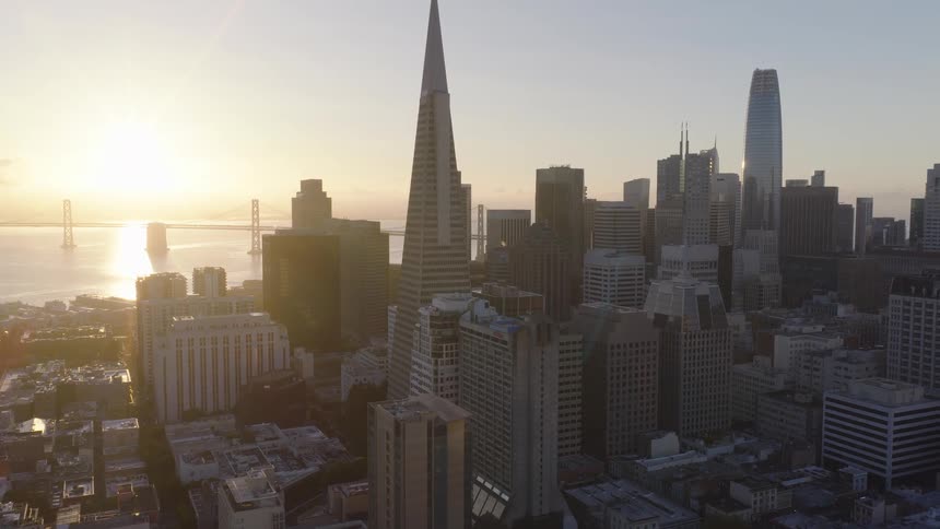 An incredible aerial view of the San Francisco skyline, featuring the Transamerica Pyramid and Bay Bridge, glows in the light of the rising sun