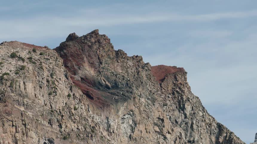 A rugged mountain peak with distinctive red and black rock formations is revealed in a slow zoom out