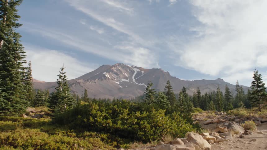 A majestic wide shot of Mount Shasta is revealed as the camera tilts down from a beautiful, cloudy blue sky