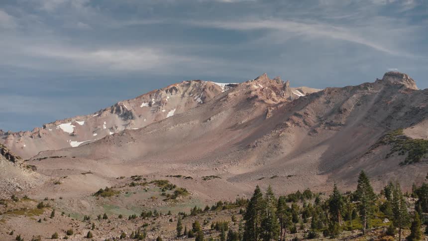A subtle zoom-in shot of a vast and desolate mountain range with patches of snow and scattered evergreen trees