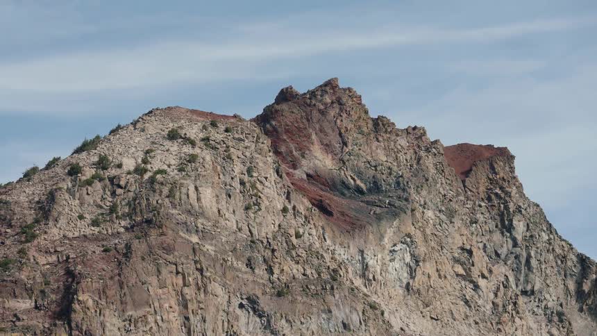 A slow zoom-in shot reveals the detailed, rugged rock face of a majestic mountain summit against a blue sky
