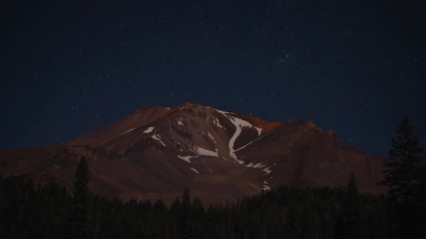 A stunning night time-lapse shows stars moving across the sky above a snow-capped mountain range and a dark forest