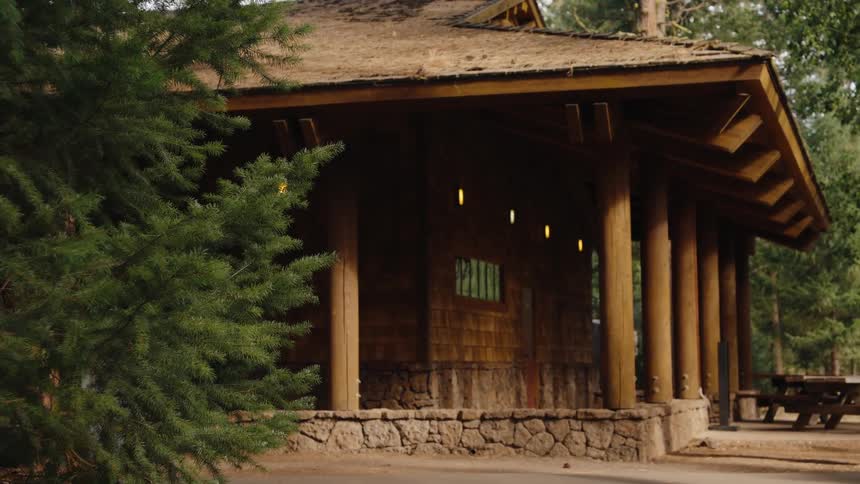A rustic wooden cabin with a stone foundation stands peacefully in a tranquil forest campground setting
