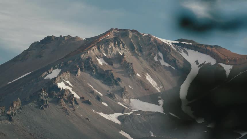 A static shot captures the rugged, snow-dusted peak of a majestic mountain illuminated by soft light