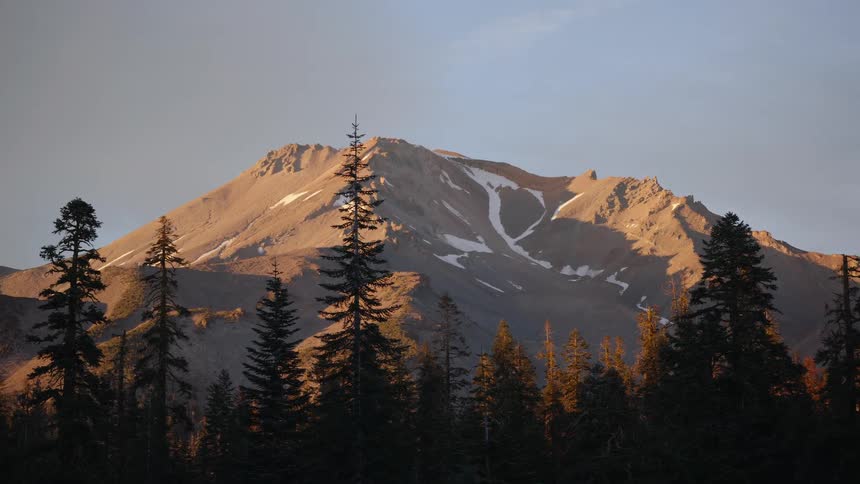 The sun rises over the snow-capped peak of Mount Shasta, with a zoom-in shot focusing on the pine trees in the foreground
