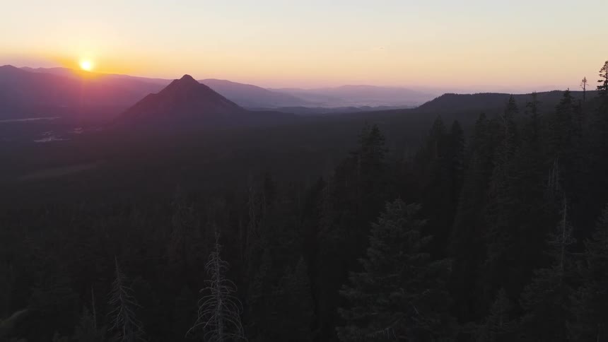 An aerial view of a lush green forest at sunset with mountain peaks in the distance creating a beautiful landscape