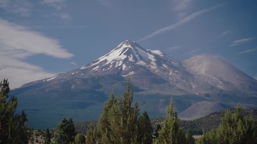 A slow zoom-out reveals the majestic, snow-capped Mount Shasta rising above a dense forest under a clear blue sky
