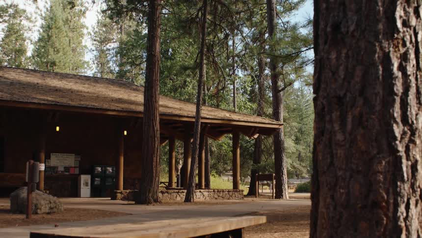 A quick motion-blurred pullback reveals a rustic wooden visitor center with a picnic table in a quiet forest campground