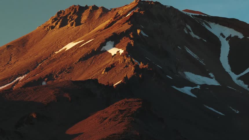The golden light of sunrise illuminates the rocky, snow-dusted peak of a majestic mountain