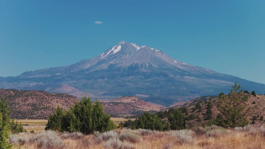 An aerial view slowly rises above the high desert to reveal the majestic, snow-capped Mount Shasta in Northern California