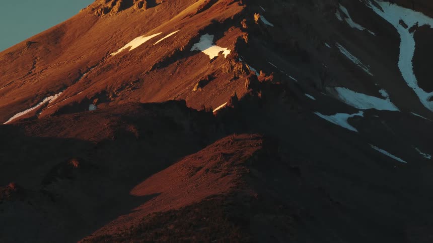 The camera tilts up to reveal a majestic, snow-capped mountain peak illuminated by the warm, golden light of sunrise