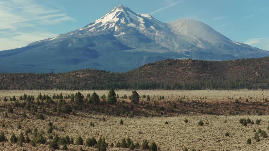 A slow zoom out reveals the majestic snow-capped Mount Shasta towering over a vast, arid valley on a clear day