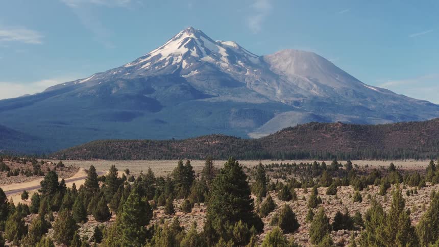 A stunning wide landscape view of the majestic, snow-capped Mount Shasta volcano on a bright, sunny day