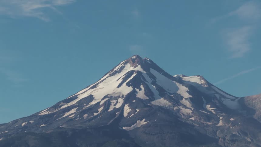 A slow zoom-out reveals the majestic snow-capped peak of a mountain towering over a lush forest under a clear blue sky