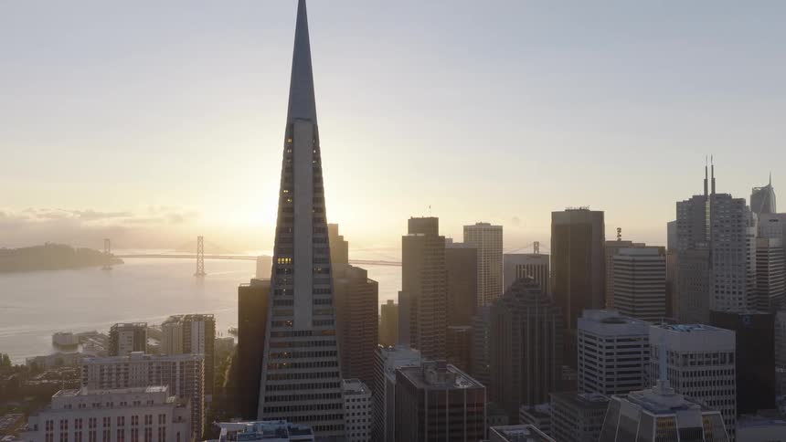 A stunning aerial view shows the sun rising over the San Francisco skyline, illuminating the Transamerica Pyramid and the Bay Bridge in the distance