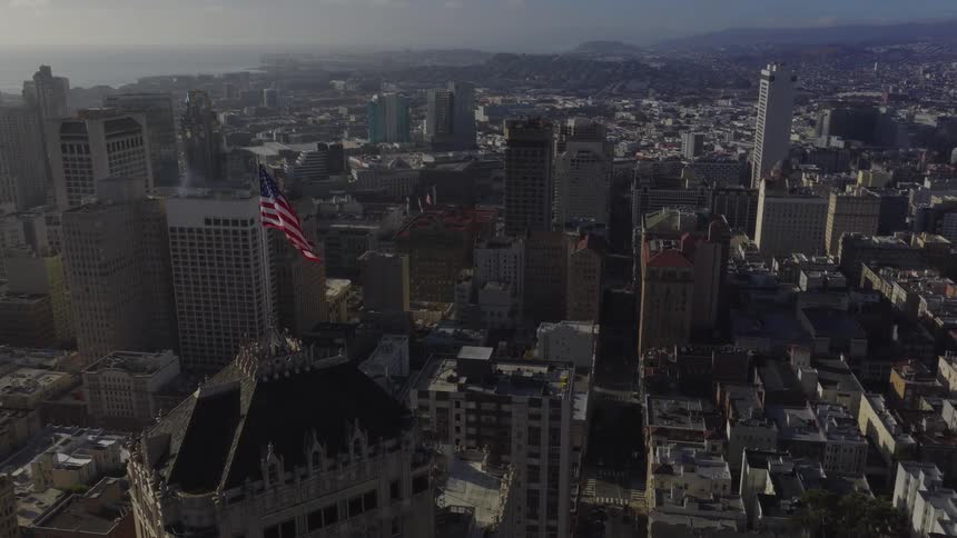 An American flag waves atop a skyscraper overlooking the sprawling San Francisco cityscape at golden hour