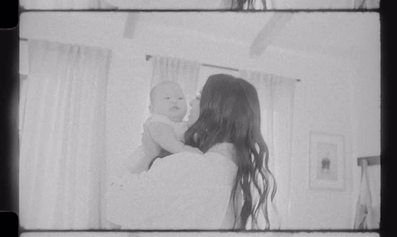 Nostalgic black and white vintage footage shows a joyful mother lifting her laughing baby into the air at home
