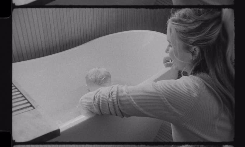 A loving mother gives her happy baby a bath in a tub, captured in a nostalgic black and white home movie style