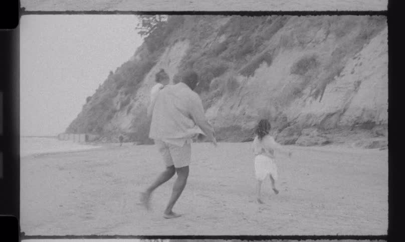 Vintage style footage of a father carrying one daughter and running along the beach with his other daughter