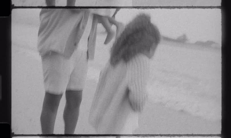 Vintage 8mm footage captures a father and his two young children sharing a tender moment on the beach by the ocean