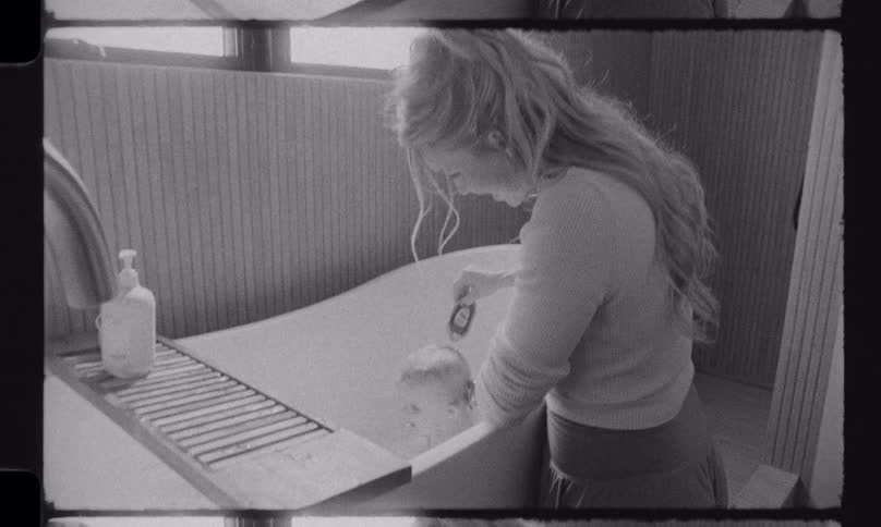 Nostalgic black and white footage shows a mother lovingly giving her baby a bath in a modern tub