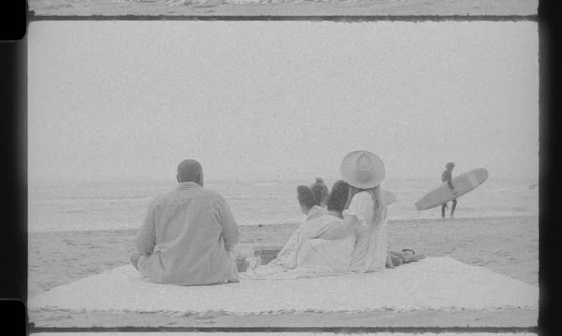 Vintage black and white 8mm film shows a family enjoying a peaceful day on the beach, watching surfers